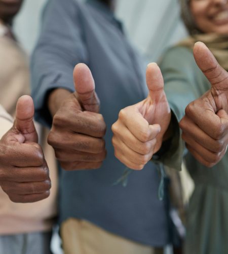 Close-up of a diverse team giving thumbs up indoors, symbolizing success and unity.